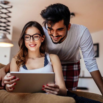 Chica sentada en un sofá mirando una tablet y chico tras ella