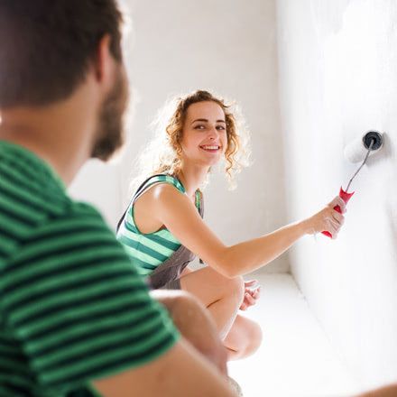 Chica pintando una pared con un rodillo que mira cámara