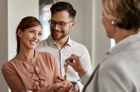 Pareja recibiendo unas llaves de un piso de una agente inmobiliaria
