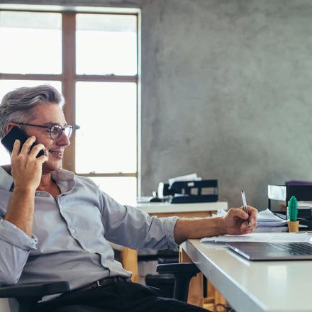 Hombre hablando por el móvil sentado en una silla frente a un escritorio
